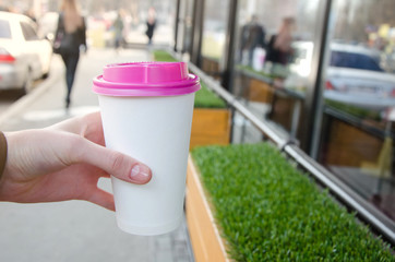 Mock up paper cup of coffee for branding .Cup of coffee with violet cap in woman's hand against green background. Good morning concept. Empty space for inscription.