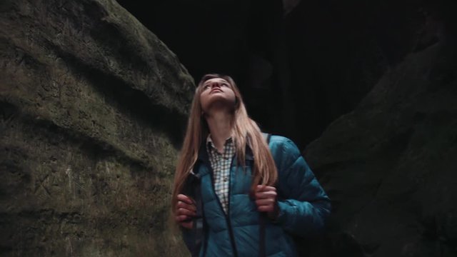 Attractive European woman, tourist with a backpack walking in the dark cave, spinning inside it, observing the surroundings. Extreme vacation, adventure. Amazing nature.