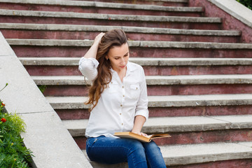 Young woman sitting on stairs with book. Hispanic girl reading book outdoor