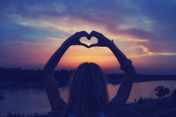 Silhouette of a girl making a heart-shape.