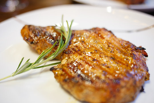 Close up image of beef steak on white plate with a twig of rosemary. Restaurant or steak-house menu background