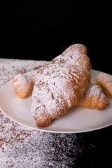 Croissants with powdered sugar and chocolate on white plate on black background. Close up
