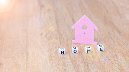 HOME word of cube letters in front of lilac coloured house symbol on wooden surface