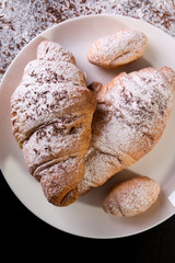 Croissants with powdered sugar and chocolate on white plate on black background. Top view. Copy space