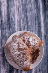 Croissants with powdered sugar and chocolate on white plate on colored wood background. Top view. Copy space