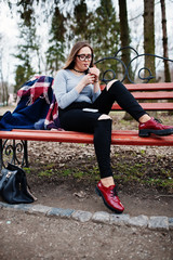 Young girl smoking cigarette outdoors sitting on bench. Concept of nicotine addiction by teenagers.