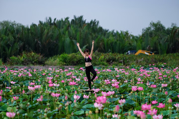Young healthy woman practicing yoga on the lotus lake at the sunrise