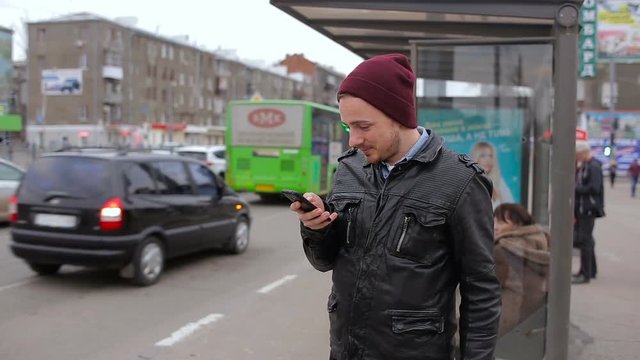 Attractive man looking at mobile phone while waiting in city bus stop