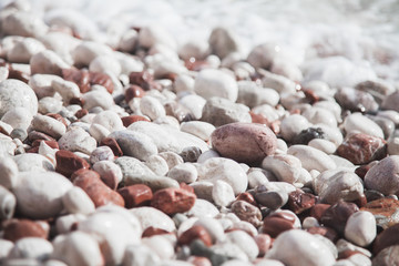 Pink, white, gray, brown pebble, stones are on beach by sea.