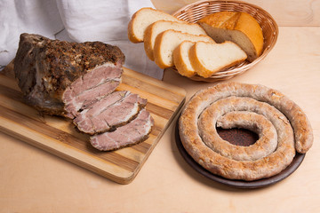 Roasted traditional homemade sausage with spices and herbs. Baked pork with herbs and spice on wooden board and and slices white wheat bread.