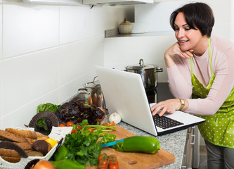 Portrait of  housewife in apron with laptop at kitchen