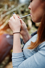 Young girl lighting cigarette outdoors close up. Concept of nicotine addiction by teenagers.