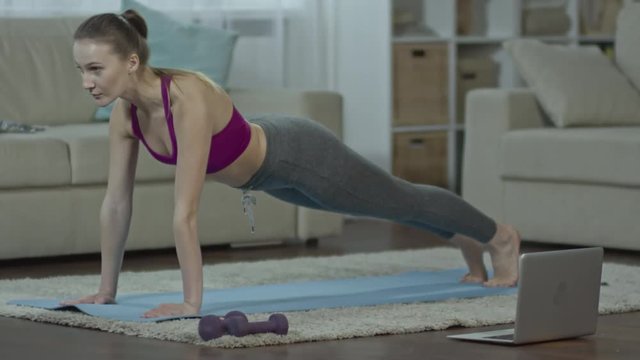 Beautiful woman doing plank pose on yoga mat on the floor in the living room