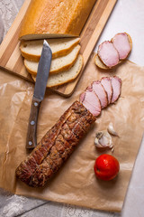 Slices smoked meat or ham and knife on brown packing paper. Tomatoes, garlic and small snacks of bread and meat.