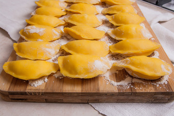 Ready for boiling vareniki, dumplings, pierogi on wooden cutting board with flour and wooden...