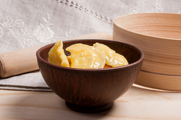 Fresh boiled varenyky or dumpling with cottage cheese or curd in clay bowl on wooden background.