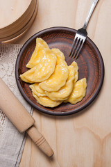 Fresh boiled varenyky or dumpling with cottage cheese or curd on clay plate and metal fork on wooden background..