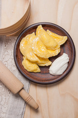Fresh boiled varenyky or dumpling with cottage cheese or curd on clay plate and with sour cream on wooden background..