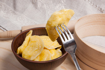 Close up view of boiled varenyky or dumpling with cottage cheese or curd on metal fork. Fresh boiled homemade ukrainian dumplings in clay bowl on wooden background..