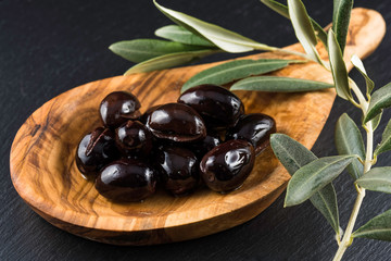 Black olives in wooden spoon and olive branch