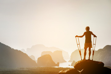 Disabled man with crutches on big rock stands like winner