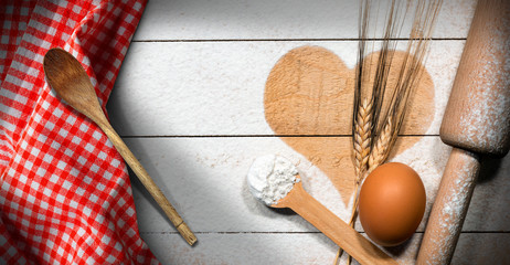 Baking background with heart of flour on a wooden table with egg and ears of wheat