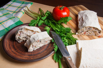 Two pieces of pita bread or lavash roll with cottage cheese or curd, chicken, tomatoes and herbs - dill, onion, parsley on brown clay plate..