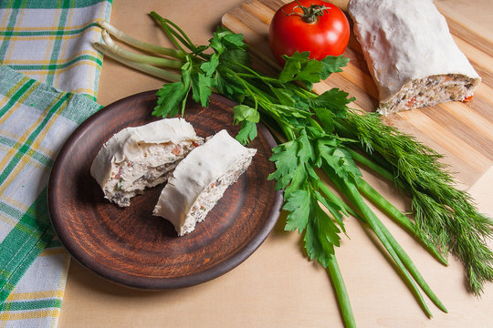 Two pieces of pita bread or lavash roll with cottage cheese or curd, chicken, tomatoes and herbs - dill, onion, parsley on brown clay plate..