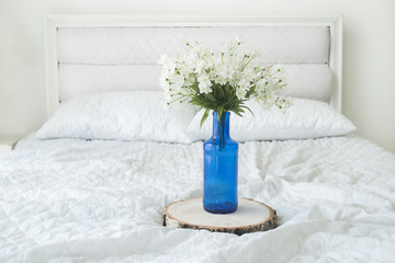 Room interior with white flowers in blue vase on white bed