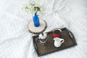 Cup of coffee with a blue vase on a wooden tray on white bed
