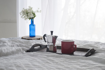 Cup of coffee with a blue vase on a wooden tray on white bed