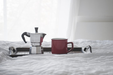 Cup of coffee with kattle on a wooden tray on white bed