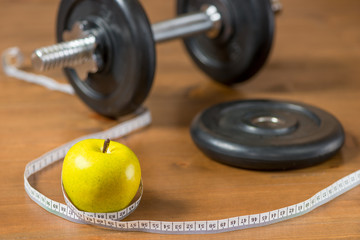 A green apple is wrapped in a centimeter against the background of a heavy dumbbell on a wooden...