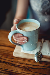 young girl with nice hands with white French manicure holding a blue vintage cup of coffee