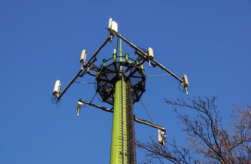 Steel telecommunication tower with antennas over blue sky and trees