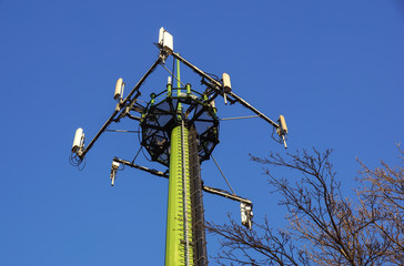 Steel telecommunication tower with antennas over blue sky and trees