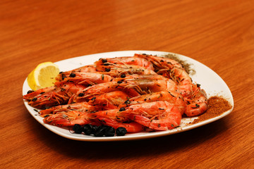 Freshly prepared shrimps lie on a white plate, adorned with spices and lemon. Against the background of a wooden table.