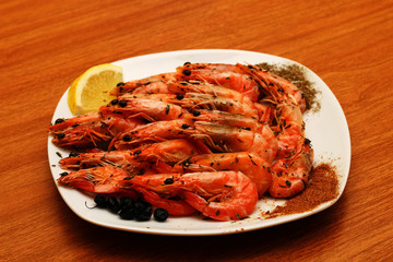Freshly prepared shrimps lie on a white plate, adorned with spices and lemon. Against the background of a wooden table.