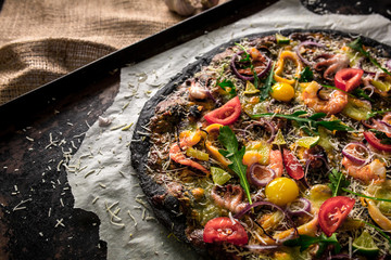 Italian pizza with black dough and seafood on a baking tray from the oven