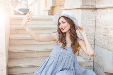 Fototapeta premium Smiling woman in hat making selfie with smartphone outdoors
