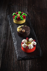 Side view on mini party tartlets with fresh fruit, chocolate, nuts and cream on black slate background