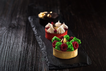 Side view on mini party tartlets with fresh fruit, chocolate, nuts and cream on black slate background