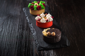 Side view on mini party tartlets with fresh fruit, chocolate, nuts and cream on black slate background