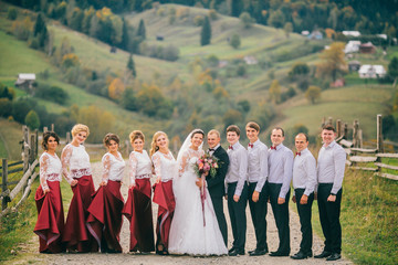 Groom hugs bride tender and kisses her cheek while they stand between bridesmaids and groomsmen....