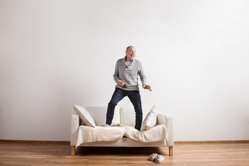 Handsome senior man standing on couch, dancing. Studio shot.