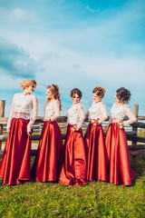Fototapeta premium Five beautiful bridesmaids in same color red dress on wedding day having fun and circling around dresses behind mountains and blue sky. Funny girls.