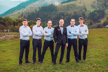 young groom and his funny friends groomsman posing for camera and having fun outdoor near mountains. Group of young men with bow tie. Cheerful friends. friends outdoors. Wedding day. 