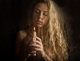 curly nude blonde woman with candle on dark background