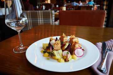 Baked potato slices and beets with vegetables and roast pork bacon on dark wooden table served in restaurant interior