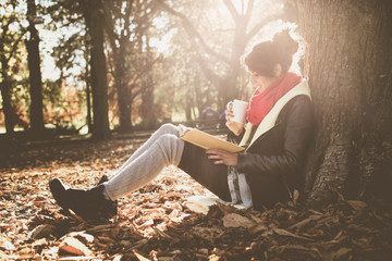  Girl leaning on a tree in the park and reading the book.